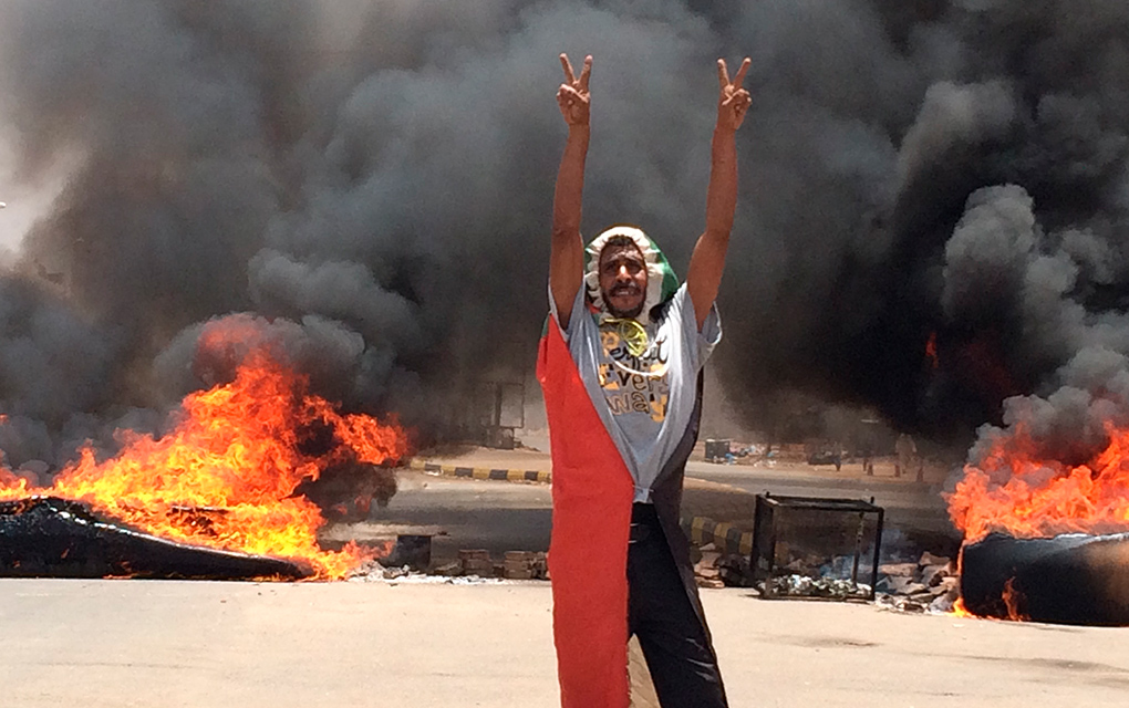 Un manifestante hace el signo de la victoria con las mano delante de neumáticos en llamas y escombros en la carretera 60, cerca de los cuarteles militares de Jartúm, la capital de Sudán / Foto: AP. 