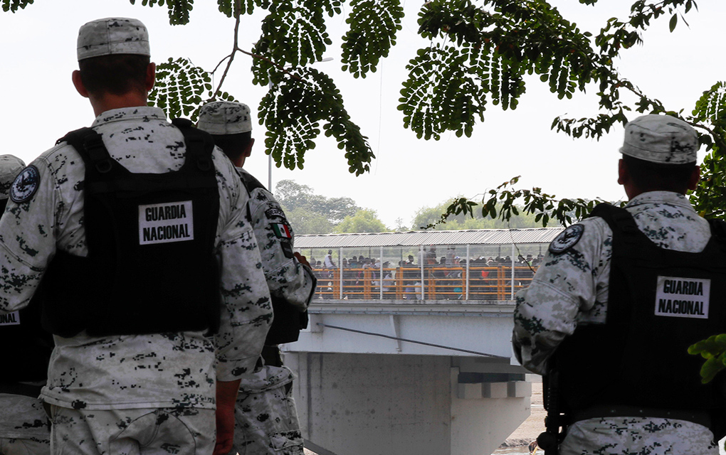 Varios efectivos de la Guardia Nacional de México observa una multitud de migrantes que pretenden cruzar un puente sobre el río Suchiate.