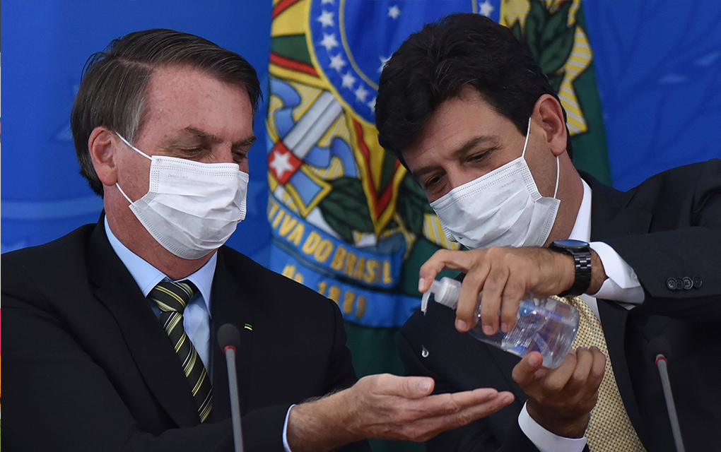El ministro de salud de Brasil Luiz Henrique Mandetta, derecha, aplica desinfectante en las manos al presidente Jair Bolsonaro durante una conferencia de prensa /AP