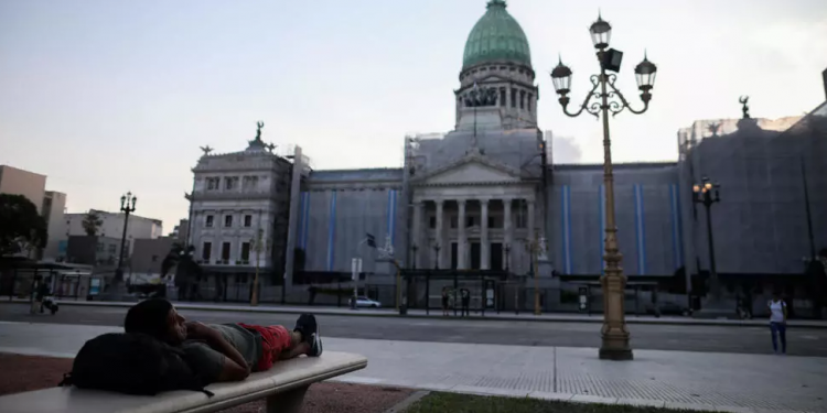 Frente al Congreso de Argentina, un joven sin casa se descansa sobre una banda. (AP)