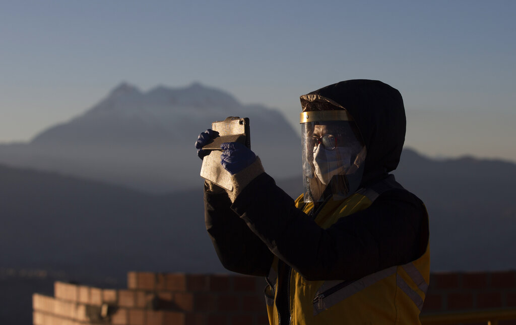 Un empleado municipal con una máscara facial en medio de la propagación del nuevo coronavirus se toma una selfie con los primeros rayos de sol durante un ritual de año nuevo en el Mirador Jach'a Apacheta de Munaypata, en La Paz, Bolivia. (AP)