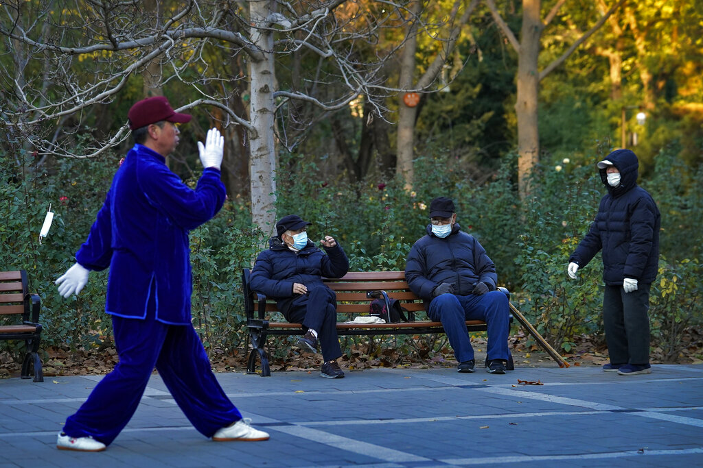 Un hombre hace ejercicio frente a otros sentados, todos con mascarillas para prevenir contagios de coronavirus, en un parque en Beijing, el lunes 23 de noviembre de 2020. (AP)
