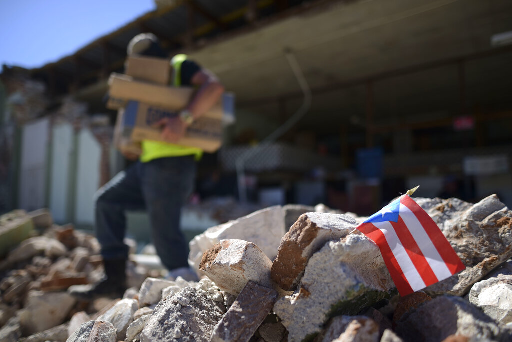 Una bandera de Puerto Rico se ve colocada entre los escombros, mientras los propietarios y familiares retiran suministros de la ferretería Ely Mer Mar, en Puerto Rico. AP