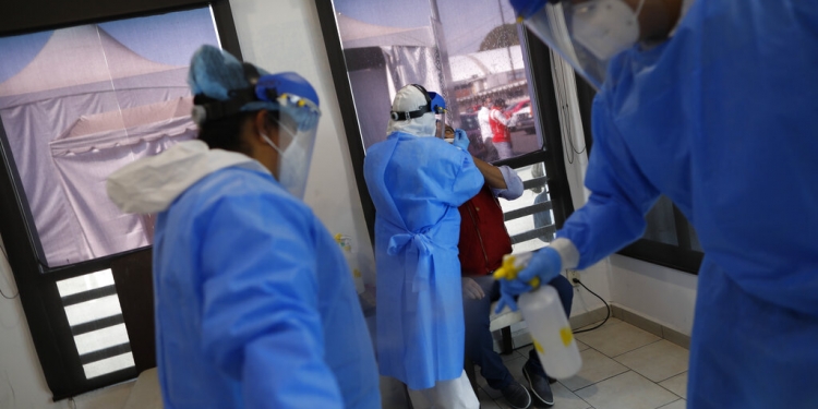 Personal médico se desinfecta mutuamente mientras un colega efectúa una prueba para detectar el coronavirus el martes 8 de diciembre de 2020 en el mercado Central de Abastos, en la Ciudad de México. (AP)