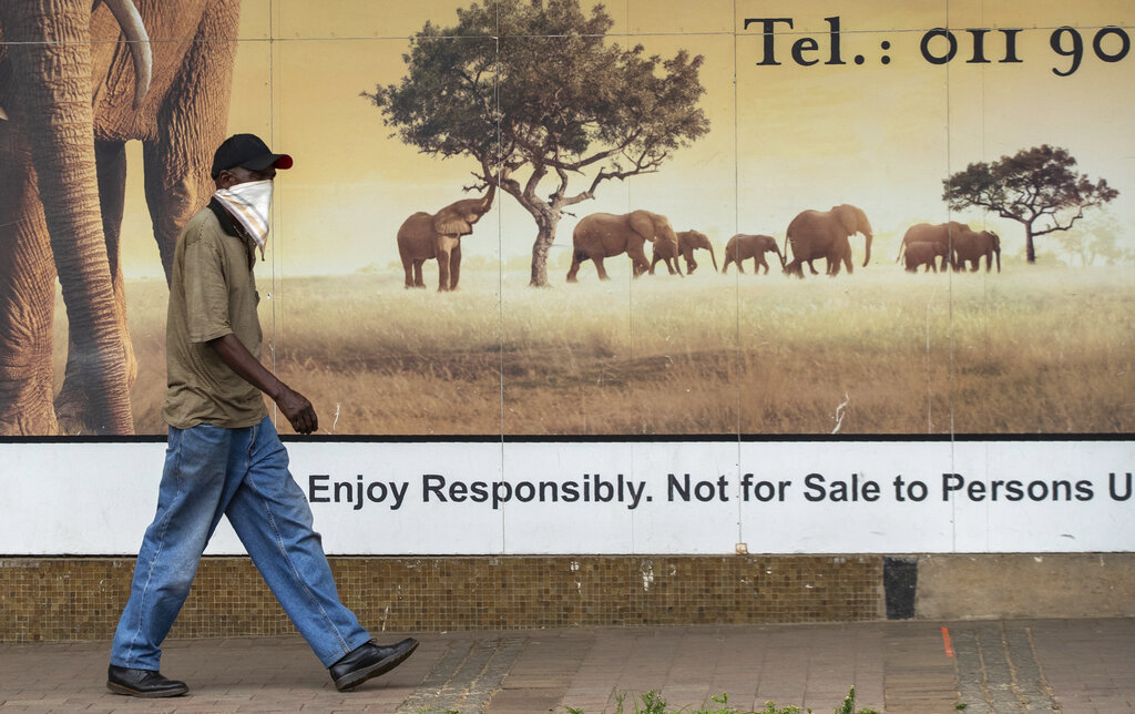 Un hombre con una mascarilla camina frente a un cartel publicitario en Alberton, cerca de Johannesburgo, Sudáfrica, el jueves 7 de enero de 2021. (AP)
