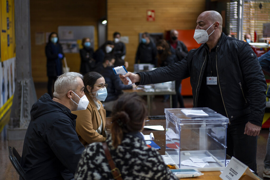Un hombre que trabaja en un centro de votación colocado en un mercado pasa un control de temperatura corporal durante las elecciones regionales en Cataluña, en Barcelona, el domingo 14 de febrero de 2021. (AP Foto/Emilio Morenatti)