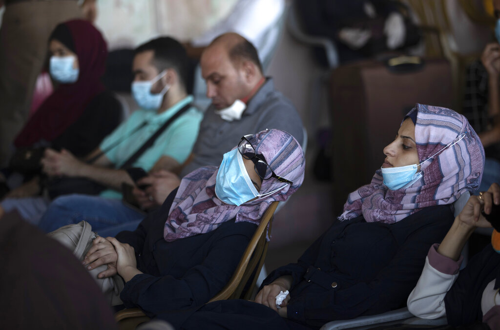 Fotografía de archivo del 27 de septiembre de 2020 de palestinos con mascarillas sentados junto a su equipaje mientras esperan cruzar el cruce fronterizo con Egipto Rafah en el sur de la Franja de Gaza. (AP Foto/Khalil Hamra, Archivo)