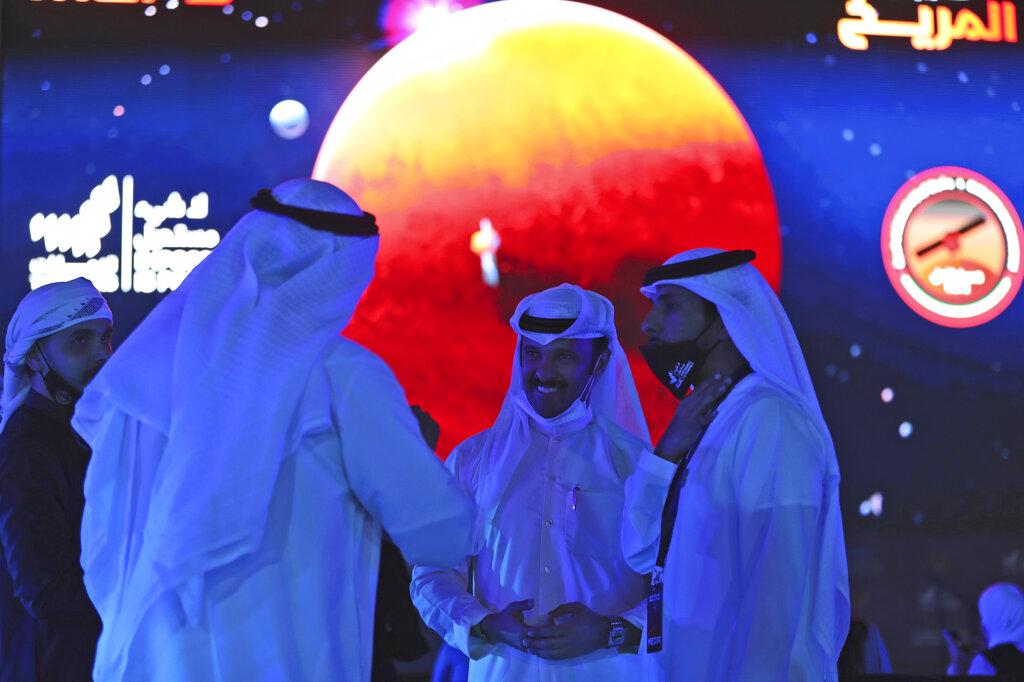 Unas personas charlan mientras a su espalda hay una pantalla que trasmitirá en vivo el trayecto de la sonda espacial Amal (Esperanza en árabe) mientras entra a la órbita de Marte, en Dubái, el 9 de febrero de 2010. (AP Foto/Kamran Jebreili)