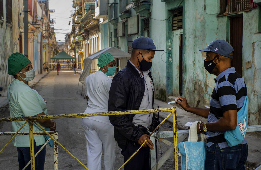 Un residente muestra su identificación a un oficial de policía que está limitando el acceso a un vecindario como una forma de frenar la propagación de la pandemia de COVID-19, mientras enfermeras están detrás en La Habana, Cuba, el lunes 22 de febrero de 2021. (AP Foto/Ramon Espinosa)