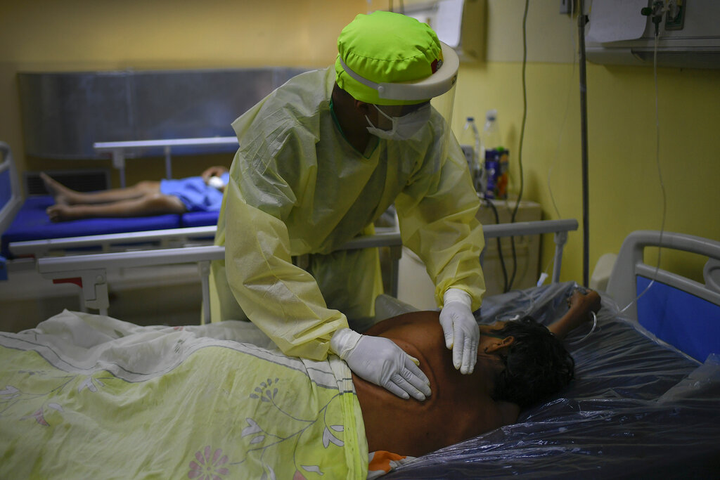 Un trabajador de salud da palmadas en la espalda a un paciente con COVID-19 el sábado 27 de marzo de 2021 en la unidad de cuidados intensivos del hospital público Ana Francisca Pérez de León II, en Caracas, Venezuela. (AP Foto/Matías Delacroix)