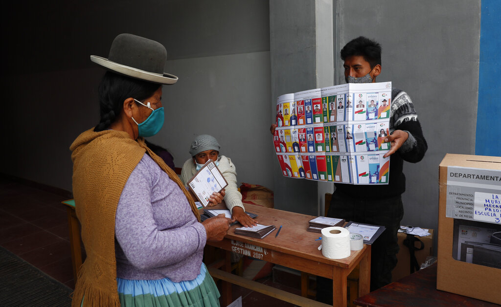 Un funcionario electoral con una máscara protectora en medio de la pandemia de coronavirus muestra una boleta sin marcar, antes de entregarla a votación en un colegio electoral durante las elecciones regionales en El Palomar, Bolivia, el domingo 7 de marzo de 2021. (AP Foto/Juan Karita)