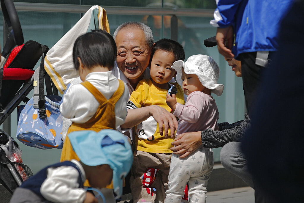 Un anciano juega con niños cerca de un edificio de oficinas en Beijing, el 10 de mayo de 2021. El gobierno chino relajará los límites de natalidad para permitir que todas las parejas puedan tener tres hijos en lugar de dos para hacer frente al rápido envejecimiento de la población, según dijo el lunes 31 de mayo una agencia estatal de noticias. (AP Foto/Andy Wong)