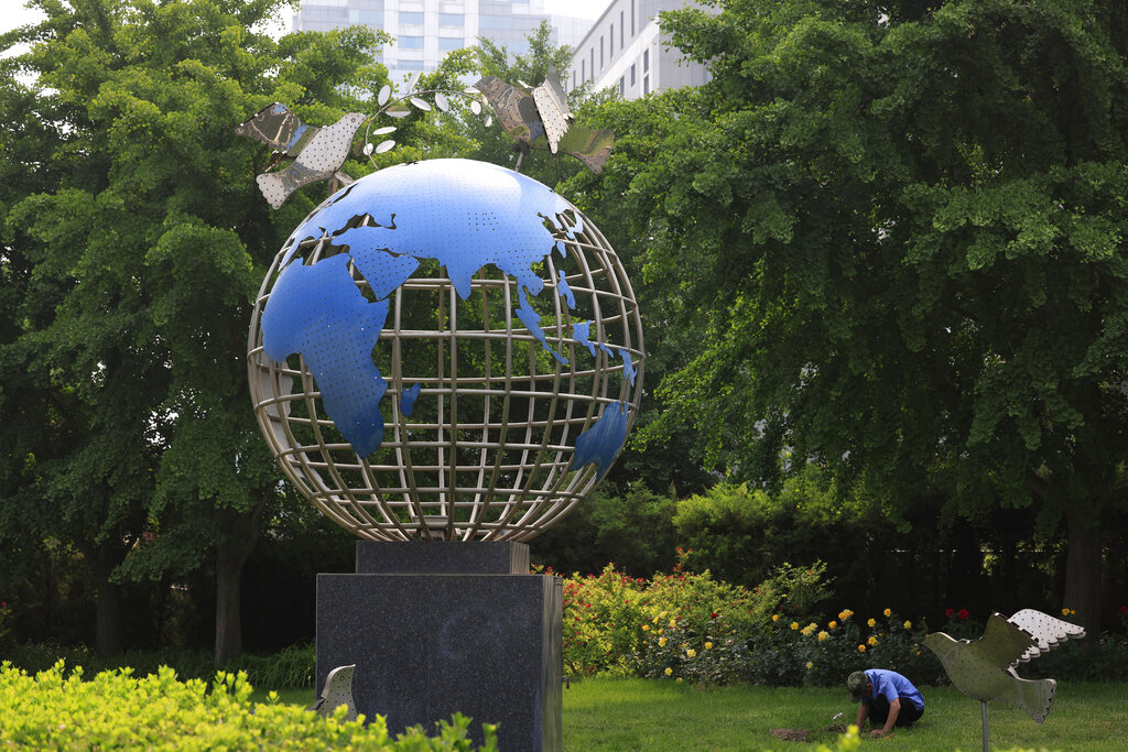 Un operario trabaja en un jardín cerca de una escultura con una réplica del globo terráqueo y palomas de la paz, en el exterior del Ministerio de Exteriores, en Beijing, el 20 de mayo de 2021. (AP Foto/Ng Han Guan)