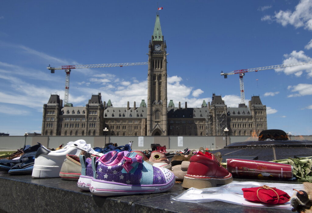 Zapatos, letreros y tabaco son colocados frente al Parlamento, en Ottawa, Ontario, el lunes 31 de mayo de 2021, en reconocimiento al descubrimiento de los cadáveres de decenas de niños en el sitio de un antiguo internado en Kamloops, Columbia Británica. (Adrian Wyld/The Canadian Press via AP)