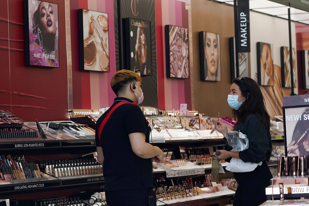 Un trabajador, a la izquierda, atiende a una clienta en una tienda de cosméticos el jueves 20 de mayo de 2021 en Los Ángeles. (AP Foto/Marcio Jose Sanchez)