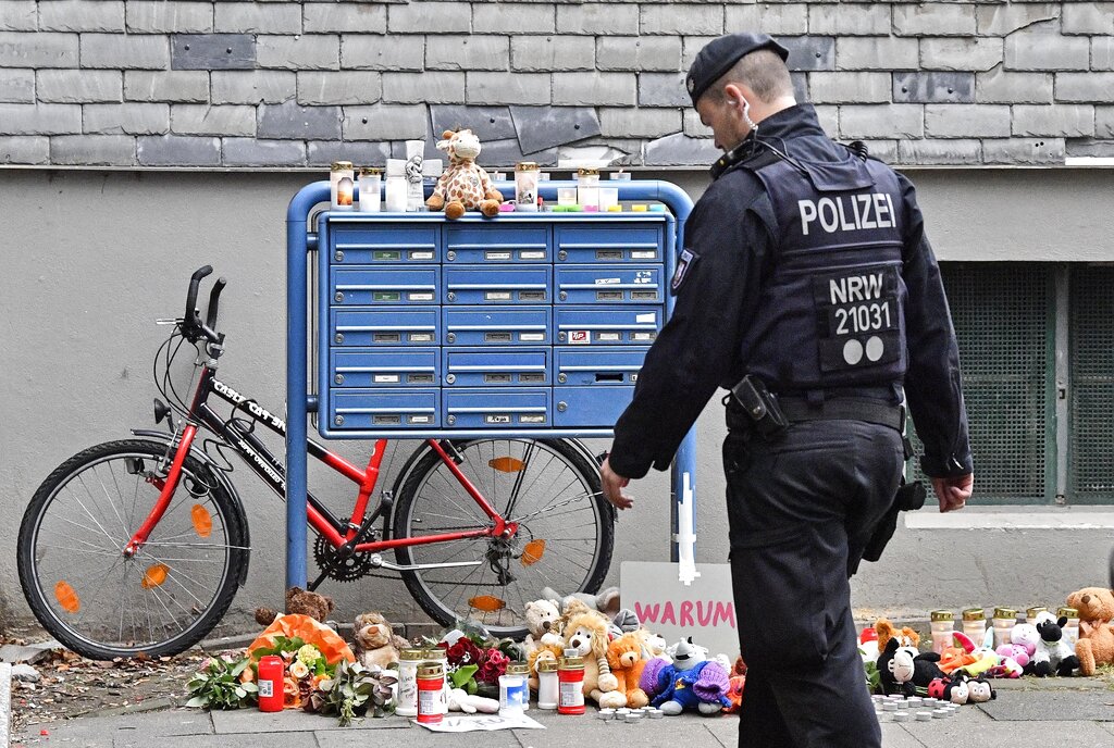 Un policía pasa frente a velas y osos de peluche en la entrada de una casa en donde cinco niños fueron encontrados muertos en Solingen, Alemania, el viernes 4 de septiembre de 2020. (AP Foto/Martin Meissner)