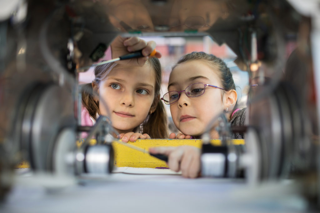 Small girls cooperating while repairing a robot in laboratory.
