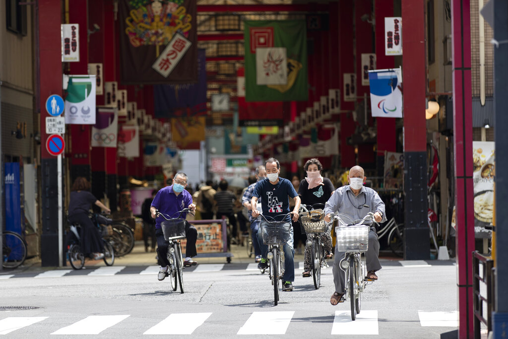 Varias personas con mascarilla cruzan un paso de peatones en bicicleta, cerca de una calle comercial, en Tokio, el 15 de julio de 2021. (AP Foto/Hiro Komae)