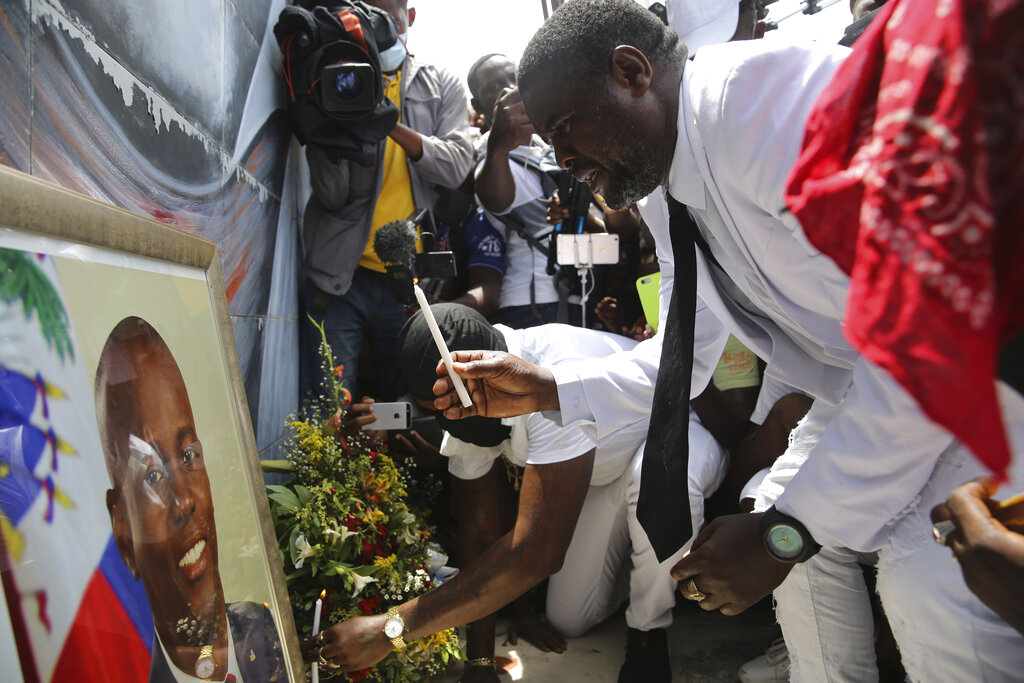 Jimmy Barbecue Cherizier, un expolicía que dirige una coalición de bandas criminales llamada G9, enciende una vela  frente a un retrato del presidente asesinado Jovenel Moïse durante una manifestación el lunes 26 de julio de 2021 para exigir justicia, en Puerto Príncipe, Haití. (AP Foto/Joseph Odelyn)