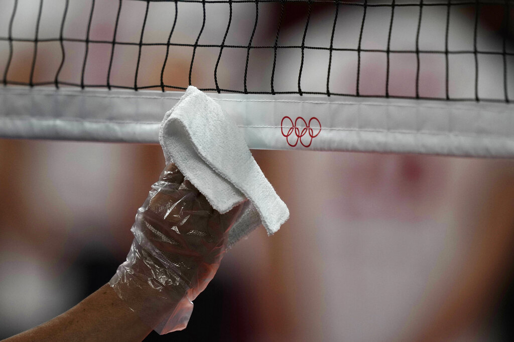 Un empleado desinfecta la red de vóleibol durante un ensayo en la arena Ariake previo a los Juegos Olímpicos de Tokio, el viernes 23 de julio de 2021. (AP Foto/Frank Augstein)