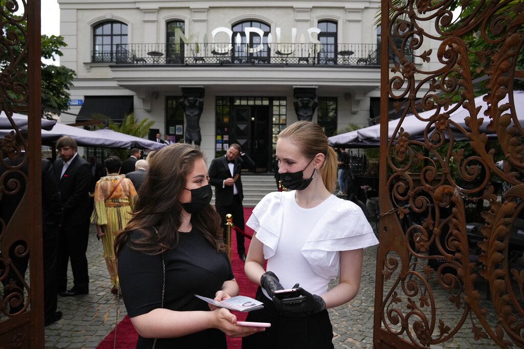 Una camarera, derecha, le da servicio a una clienta, ambas con mascarillas para protegerse del coronavirus, a la entrada de un restaurante el sábado 3 de julio de 2021, en Moscú, Rusia. (AP Foto/Alexander Zemlianichenko)
