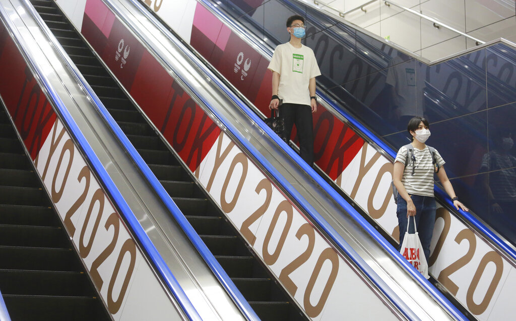 En esta foto del 7 de julio de 2021, un par de personas con mascarillas baja por elevador con banderas con el logo de los Juegos Olímpicos en Tokio. (AP Foto/Koji Sasahara)