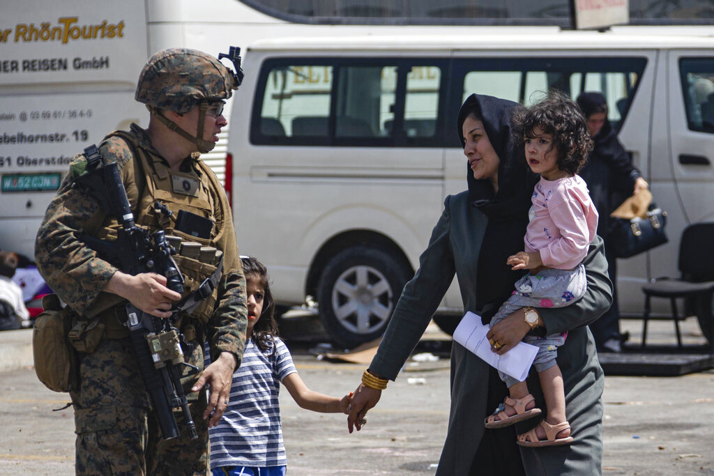 En esta imagen facilitada por el Cuerpo de Infantería de Marina de Estados Unidos, un efectivo estadounidense escolta a evacuados en el aeropuerto internacional Hamid Karzai en Kabul, Afganistán, el viernes 20 de agosto de 2021.  (Cabo Davis Harris/Cuerpo de Infantería de Marina de Estados Unidos vía AP)