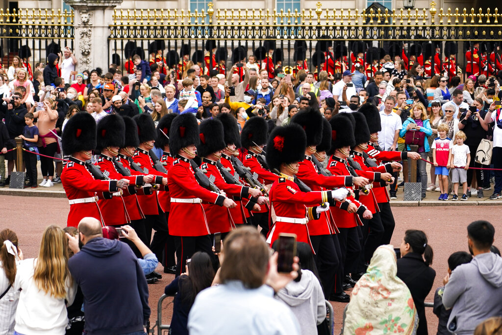 Varias personas observan la ceremonia de cambio de guardia afuera del Palacio de Buckingham, en Londres, el lunes 23 de agosto de 2021. (AP Foto/Alberto Pezzali)