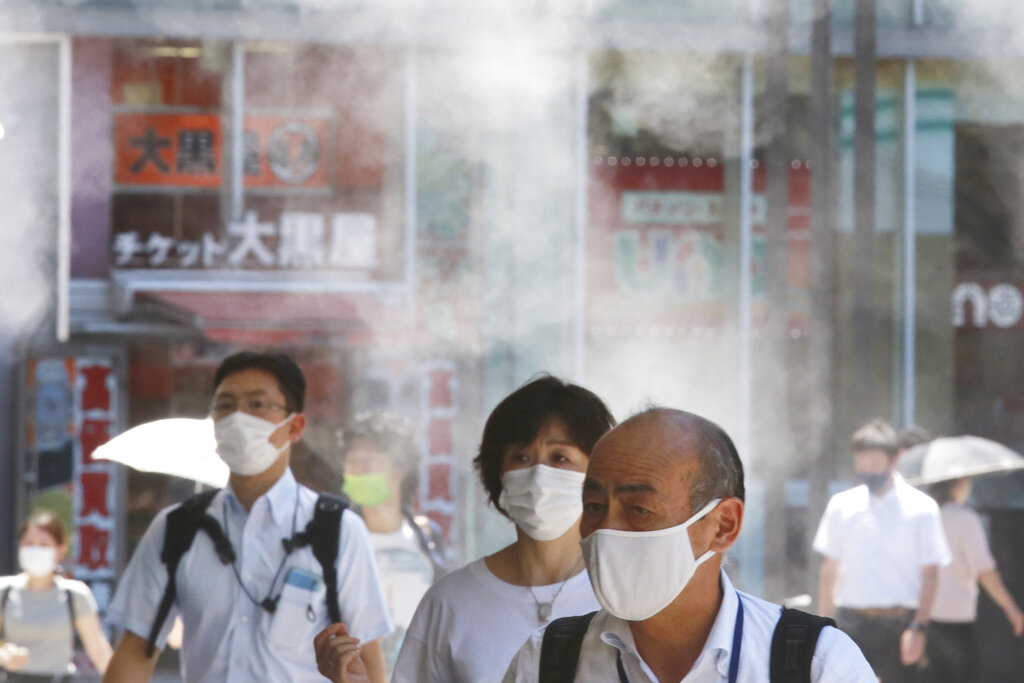 Gente con mascarillas para protegerse contra la expansión del coronavirus caminan bajo agua vaporizada en Tokio, el jueves 5 de agosto de 2021. (AP Foto/Koji Sasahara)