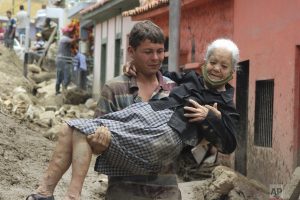 En Merida,Venezuela, un hombre carga a una anciana para cruzar una calle inundada y dañada por las lluvias torrenciales. (AP)