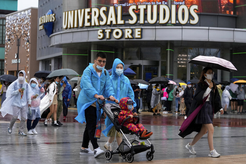 Una familia con impermeables y cubrebocas caminan frente a otros visitantes con cubrebocas formados para entrar a Universal Studios Beijing en Beijing, el 20 de septiembre de 2021. (AP)