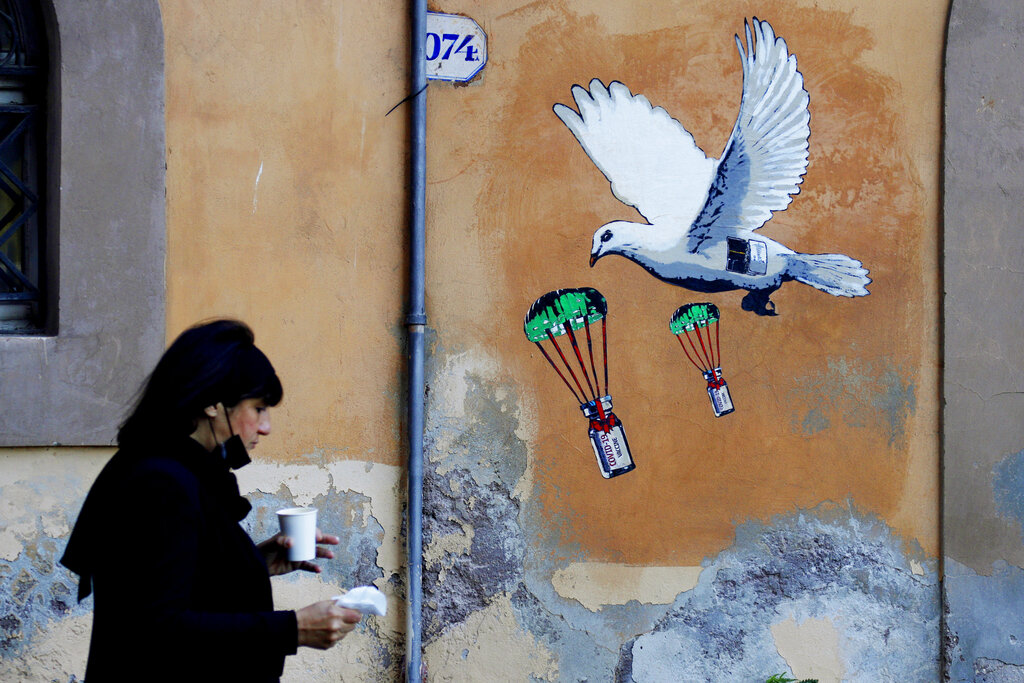 En esta imagen de archivo, una mujer pasa por delante de un mural con la imagen de una paloma blanca lanzando viales de la vacuna contra el COVID-19 en paracaídas, cerca de la sede del Ministerio de Salud de Italia, en Roma, el 4 de abril de 2021. (AP)