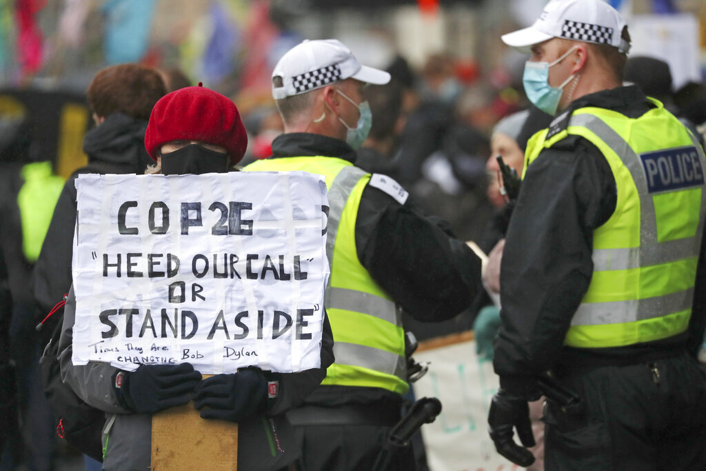 Una activista por el clima sostiene un cartel junto a policías cerca de la sede de la Conferencia de Naciones Unidas sobre Cambio Climático, o COP26, en Glasgow, Escocia, el 12 de noviembre de 2021. (AP)