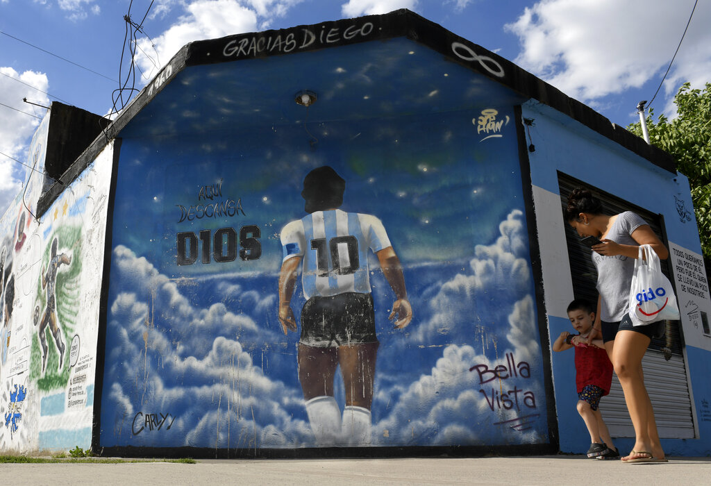 Una mujer y un niño pasan caminando frente a un mural que muestra a Diego Mardona de espaldas en el barrio Lomas de Marilo, en Buenos Aires. (AP)