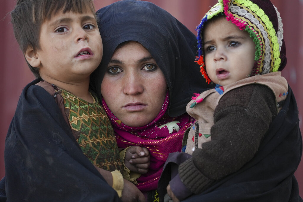 Una mujer afgana carga a sus hijos mientras espera consulta afuera de una clínica precaria en un enorme asentamiento de barracas de adobe donde viven personas desplazadas por la guerra y la sequía cerca de Herat, Afganistán, el 16 de diciembre de 2021.  (AP Foto/Mstyslav Chernov)