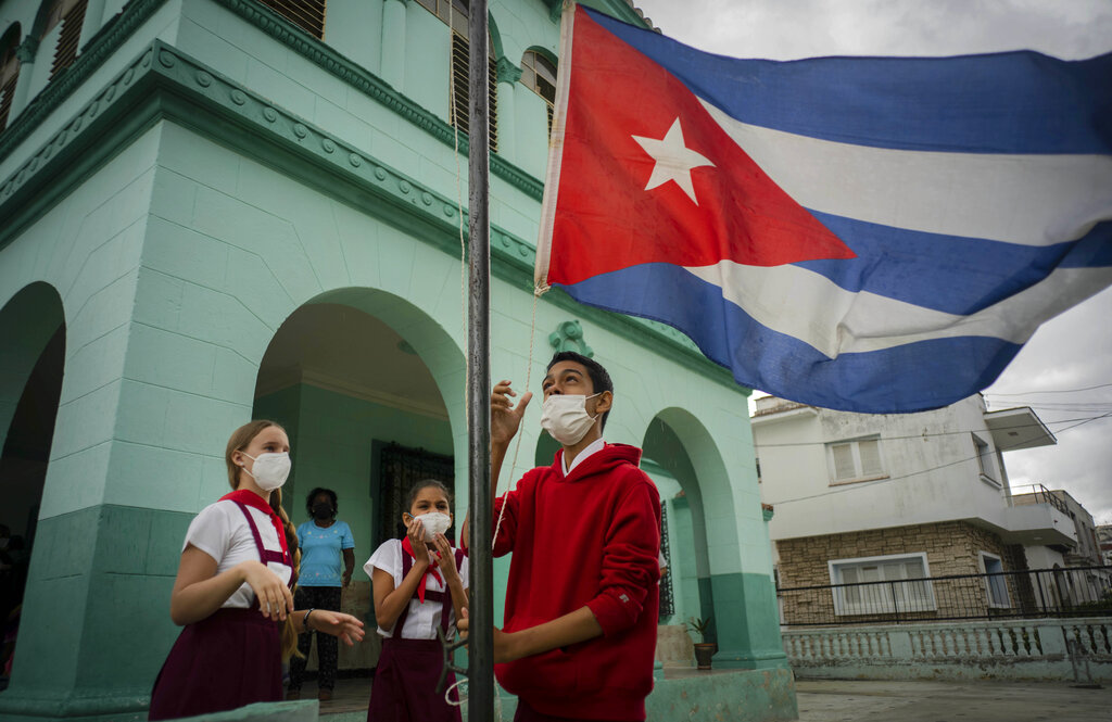 Estudiantes, con mascarilla por la pandemia del coronavirus, arrían una bandera cubana para evitar que se moje por la lluvia durante el primer día de escuela presencial en meses, en La Habana, Cuba. (AP)