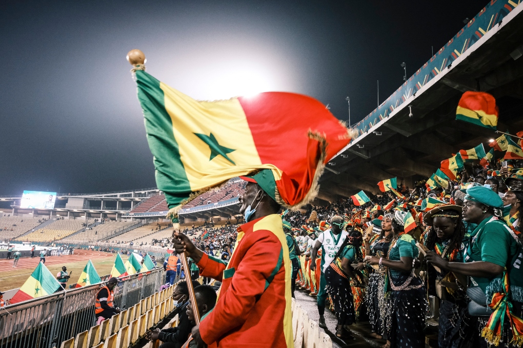 A Senegal fan waves the flag during their African Cup of Nations semifinal match with Burkina Faso, in Yaounde, Cameroon, Feb. 2, 2022. Many countries competing here are enduring security, economic and political crises, but the tournament offers visions of unity, solidarity and joy. (Tom Saater/The New York Times)