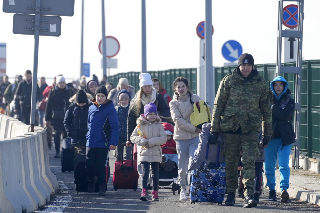 Un guardia fronterizo polaco (derecha) ayuda a los refugiados ucranianos a llegar a Polonia en el cruce fronterizo de Korczowa, Polonia, el sábado 26 de febrero de 2022. (AP)