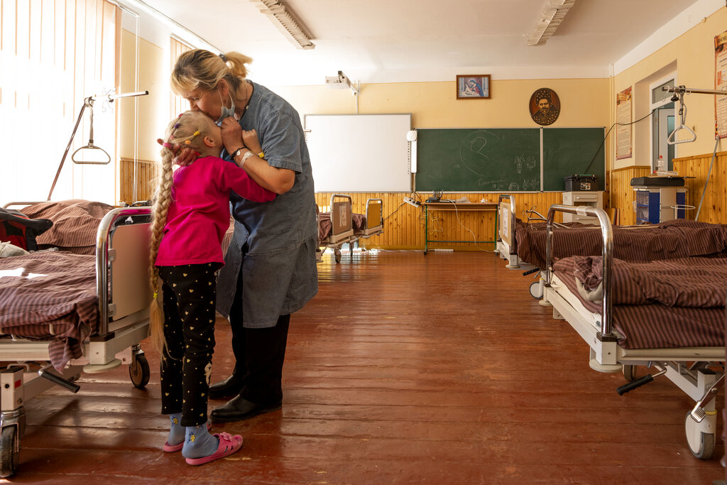 Nadia besa a su nieta de 10 años, Zlata Moiseinko, quien padece una afección cardíaca crónica, mientras recibe tratamiento en una escuela convertida en hospital de campaña en Mostyska, en el oeste de Ucrania. (AP)