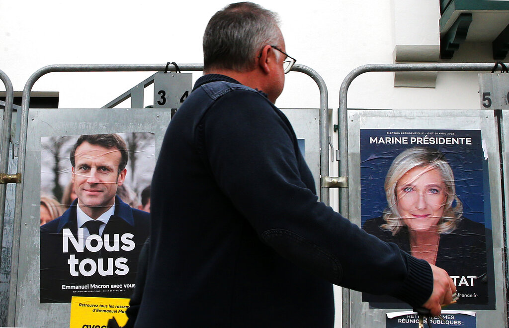 Un hombre pasa frente a dos murales del presidente francés Emmanuel Macrón, de centro, y la candidata Marine Le Pen, de extrema derecha, en Anglet, al suroeste de Francia, el miércoles 8 de abril de 2022. (AP)