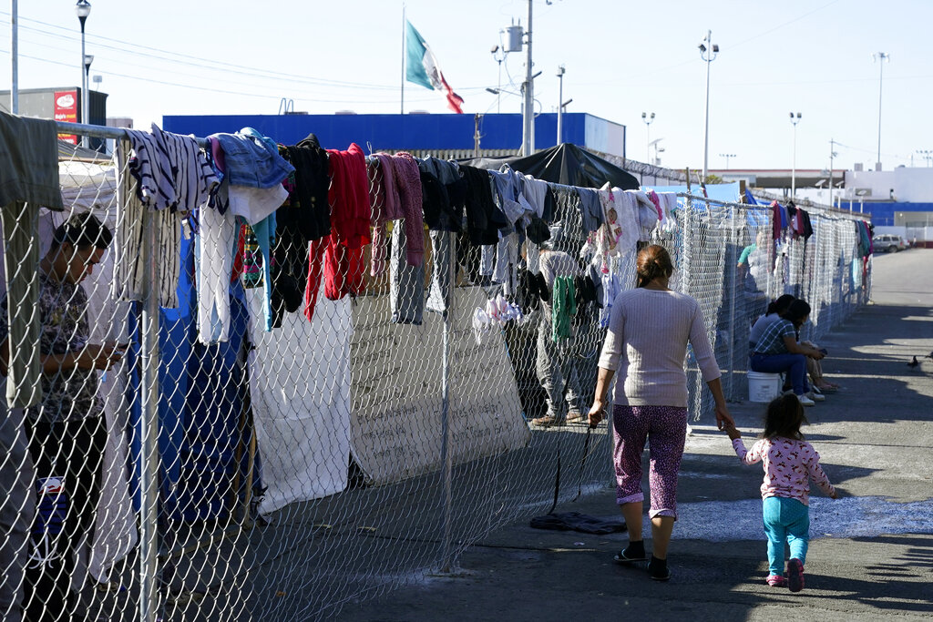 Migrantes caminan a lo largo de una cerca en un campamento improvisado que es hogar temporal de cientos de migrantes que esperan solicitar asilo en Estados Unidos en un cruce peatonal el 8 de noviembre de 2021, en Tijuana, México. (AP)